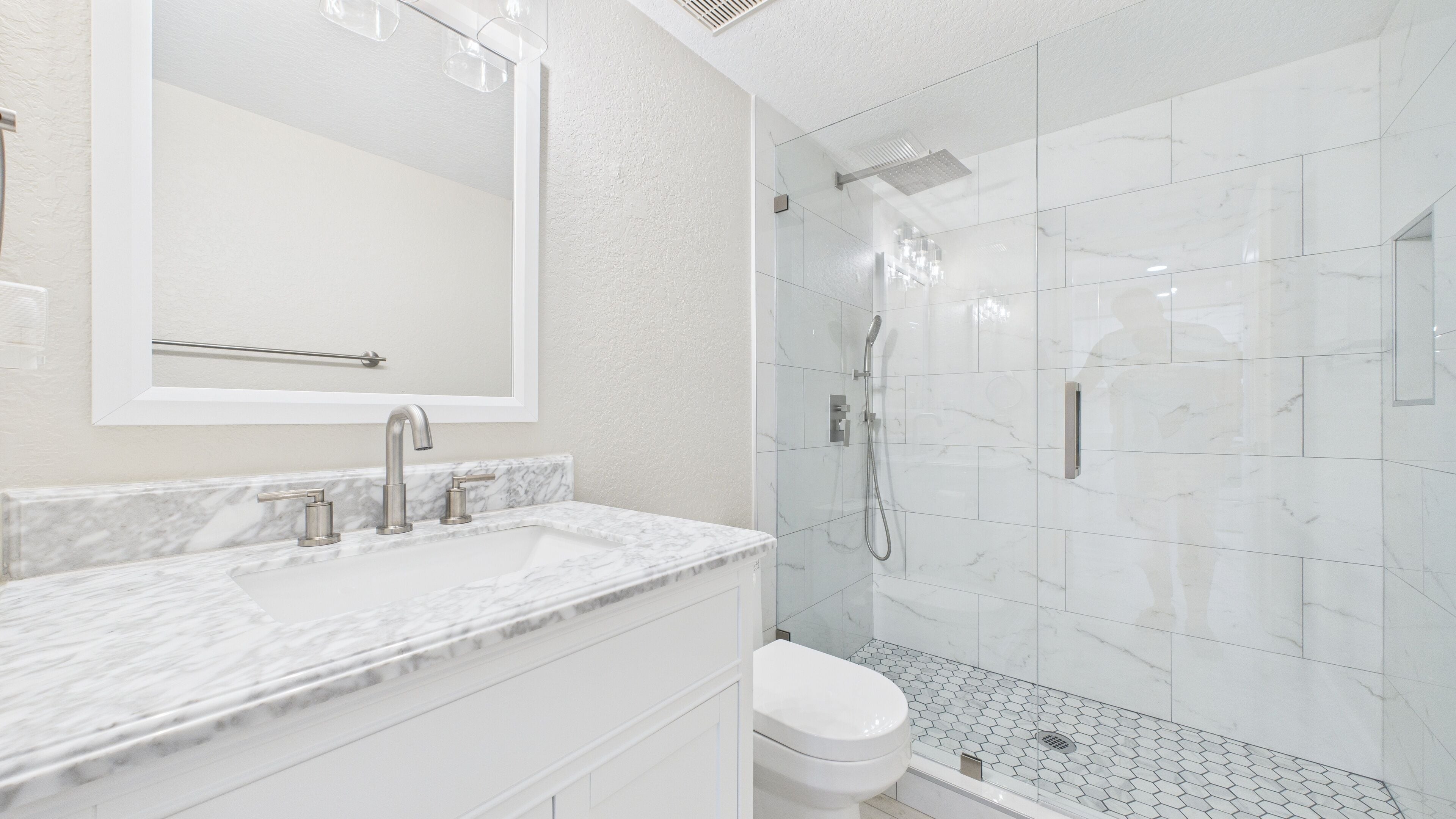 A modern bathroom with a marble sink, a toilet, and a glass-enclosed shower area.