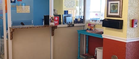 Uma área de recepção com porta de vidro, balcão e detector de incêndio na parede.