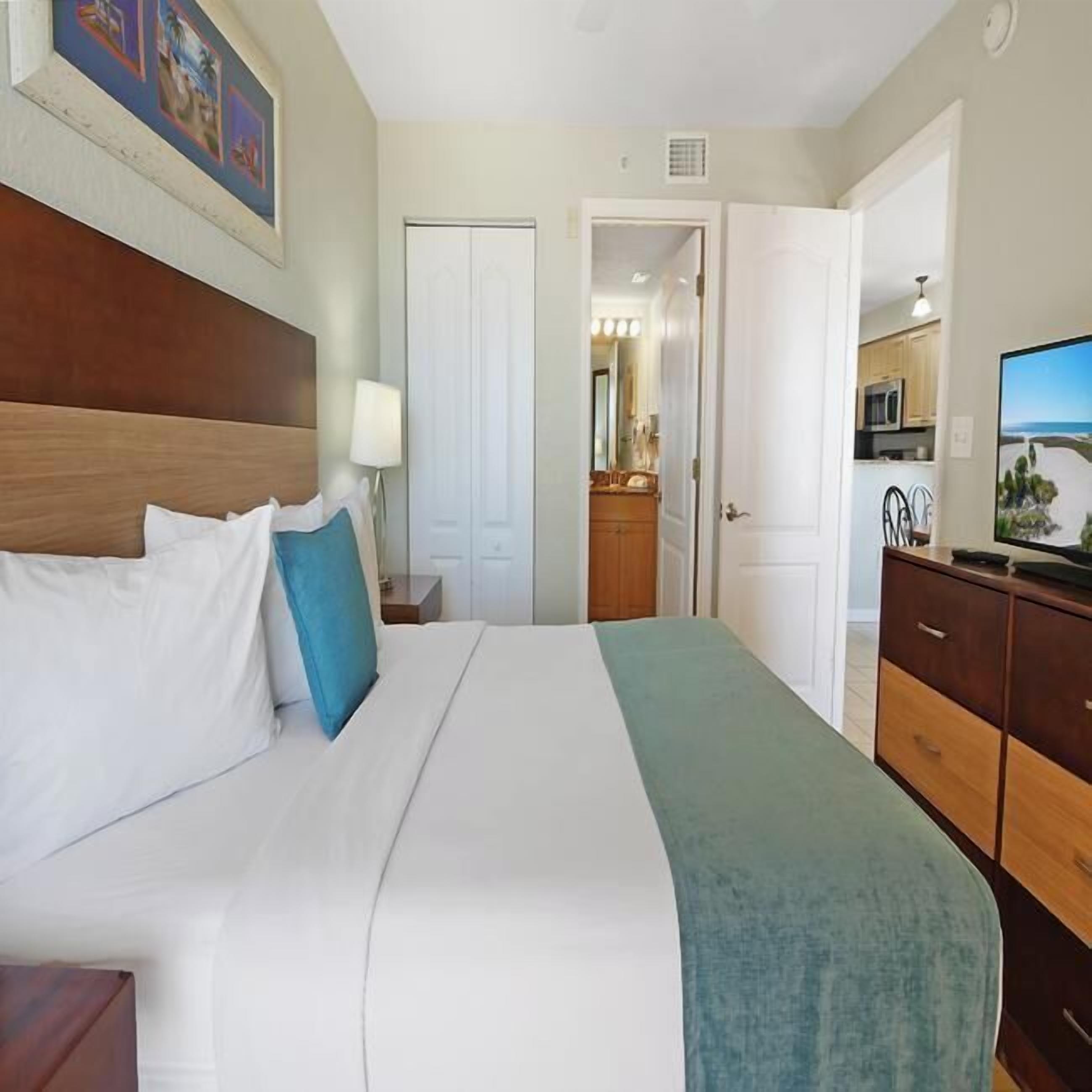 A hotel room with a bed, a dresser, a mirror, and a television.