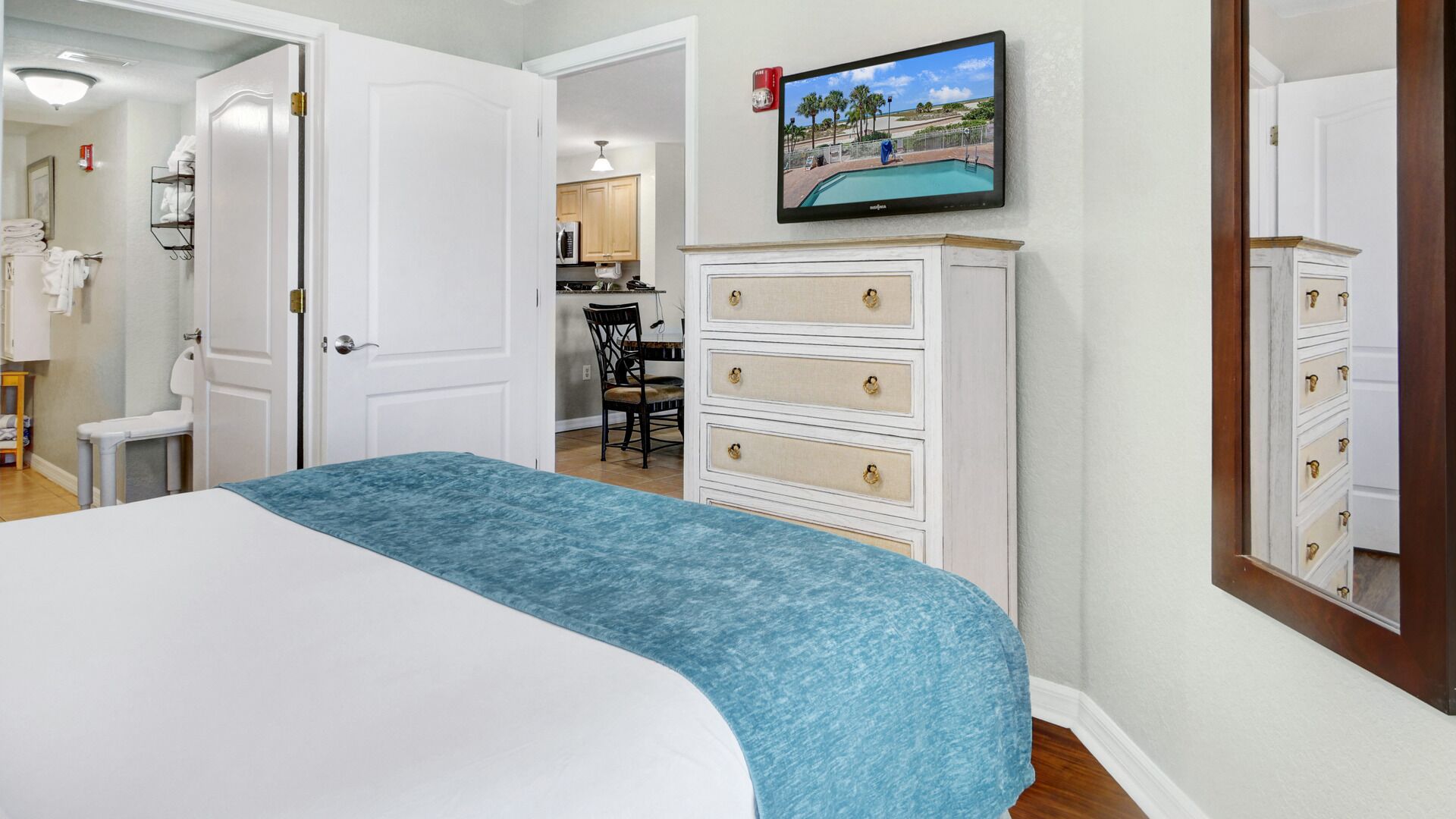 A bedroom with a bed, a dresser, a television mounted on the wall, and a view of a pool through the window.