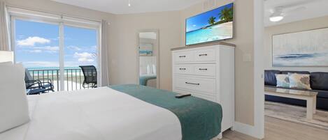 Habitación de hotel con cama, televisor, balcón y vistas a la playa, además de un sofá.
