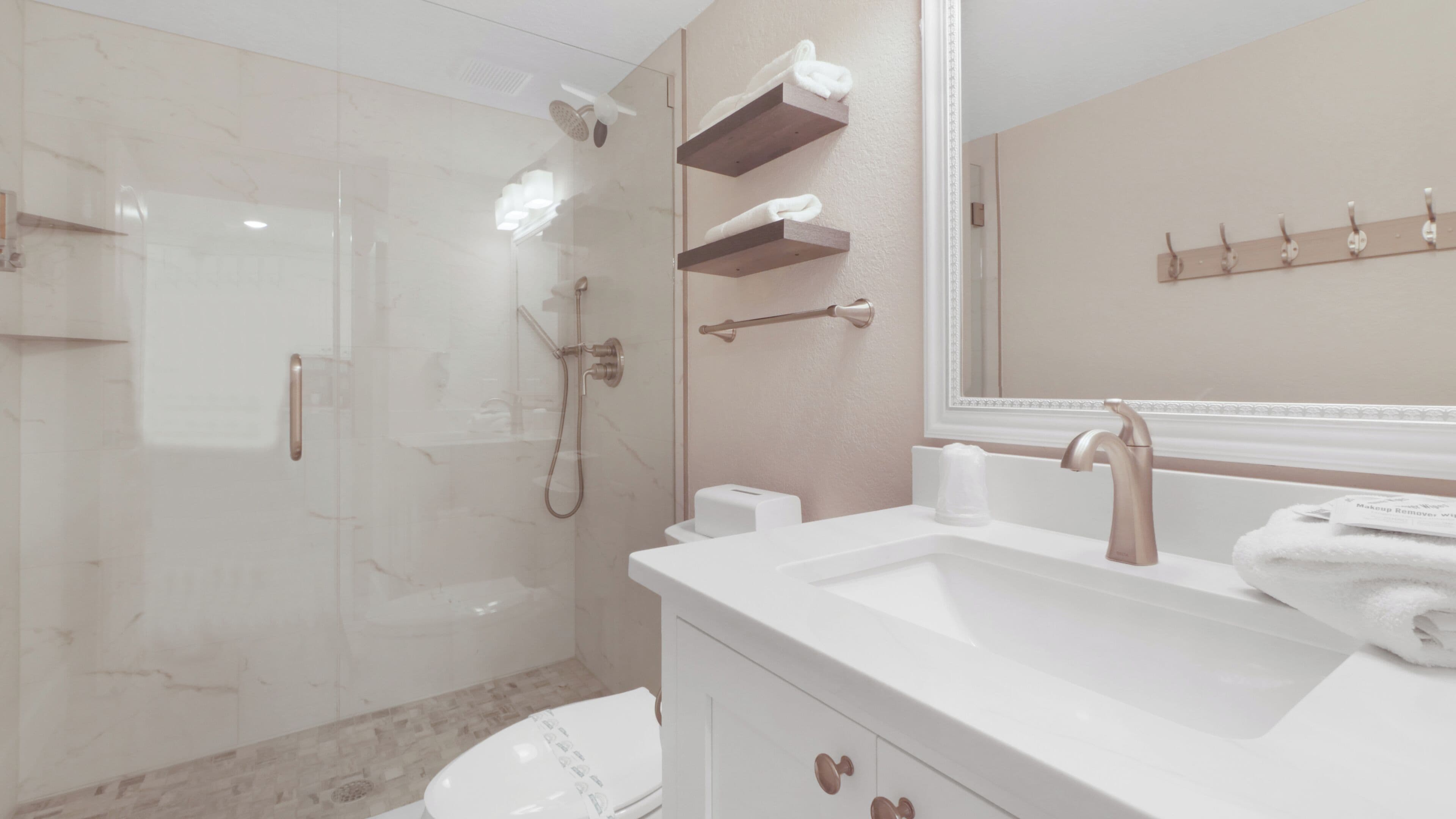 Un bany modern amb plat de dutxa envoltat de vidre, un lavabo blanc i un mirall gran, i prestatges de fusta a sobre del mirall.