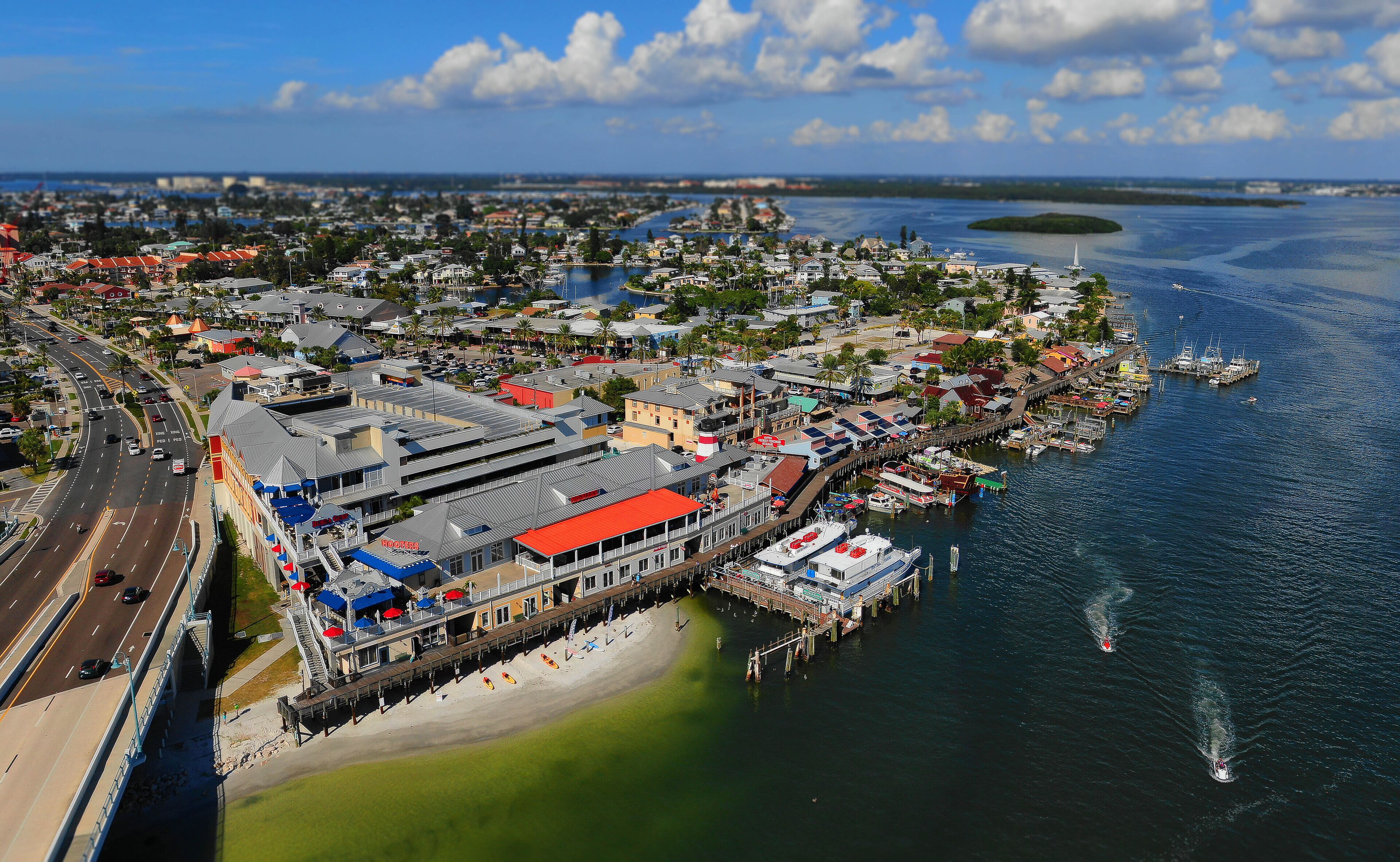 An aerial view of a coastal town with a prominent waterfront area featuring a pier, boats, and a beach.