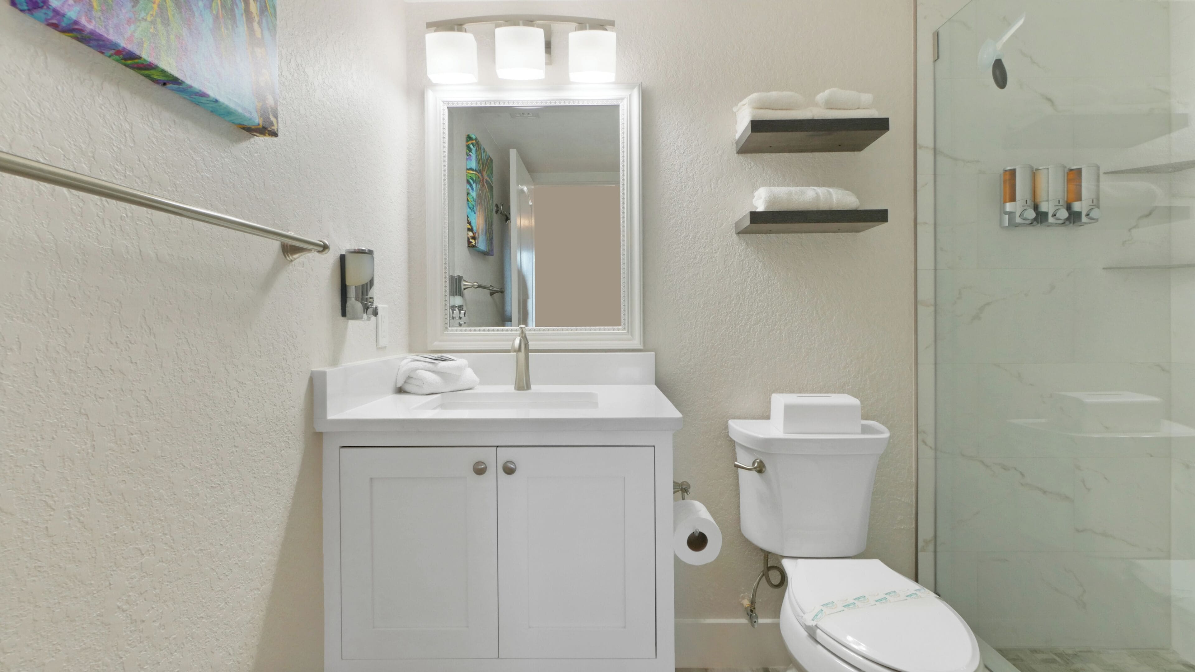 Une salle de bain avec un meuble-lavabo blanc, des toilettes, une cabine de douche en verre et un miroir au-dessus du lavabo.
