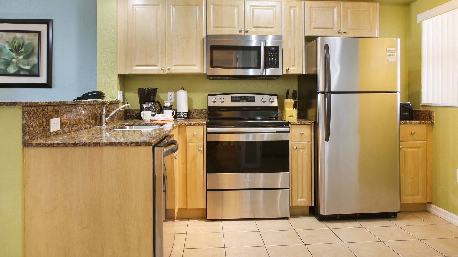 A compact kitchen with wooden cabinets, a stainless steel refrigerator, a microwave, and an oven.