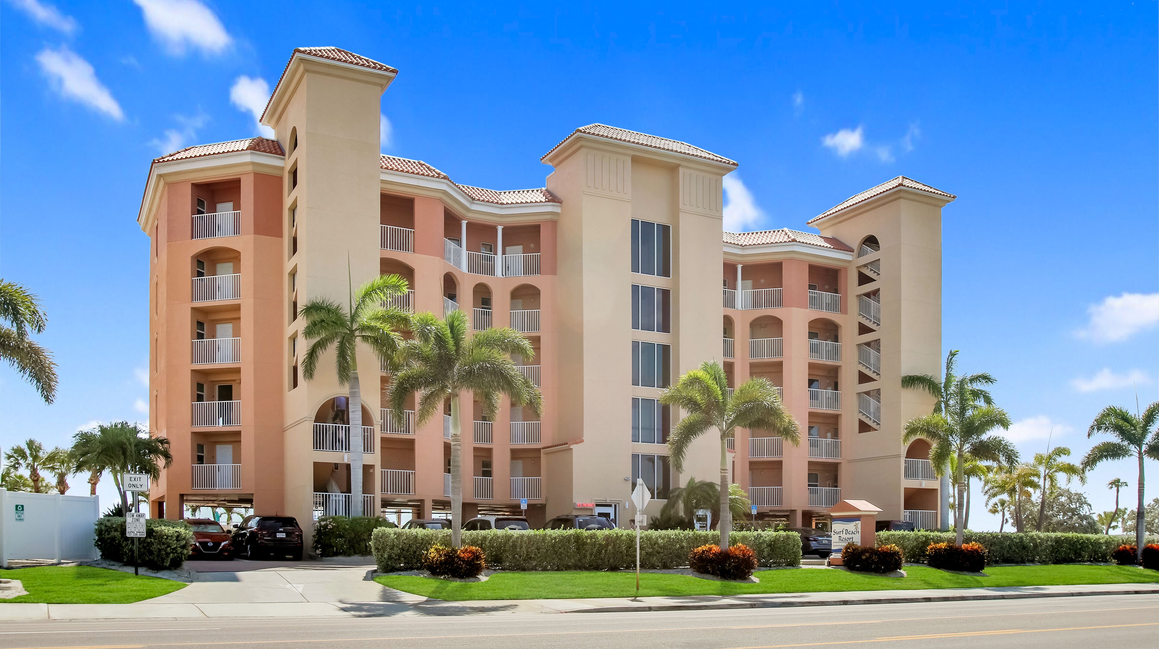 A multi-story hotel with balconies, palm trees, and a clear blue sky.