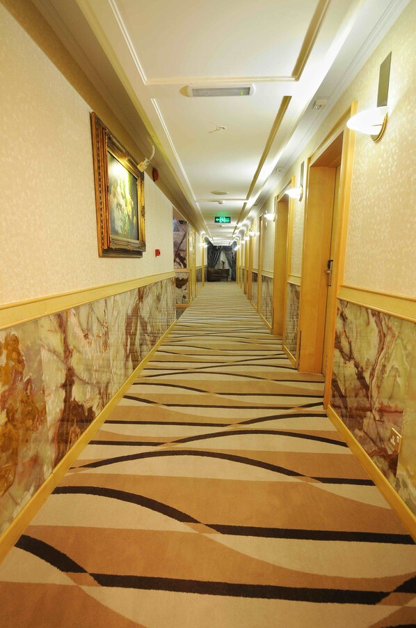 A hotel corridor with patterned carpet, marble walls, and doors leading to rooms.