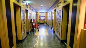 Un pasillo de hotel con puertas de madera, suelo de mármol y sillas rojas.