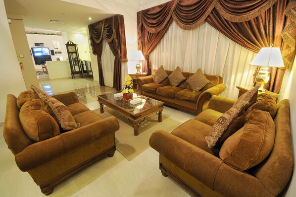 A spacious living room with two sofas and a coffee table, a TV in the background, and a clock on the wall.