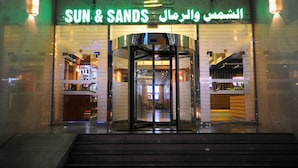La entrada de un hotel con puerta giratoria, puertas de cristal y señalización iluminada en inglés y árabe.