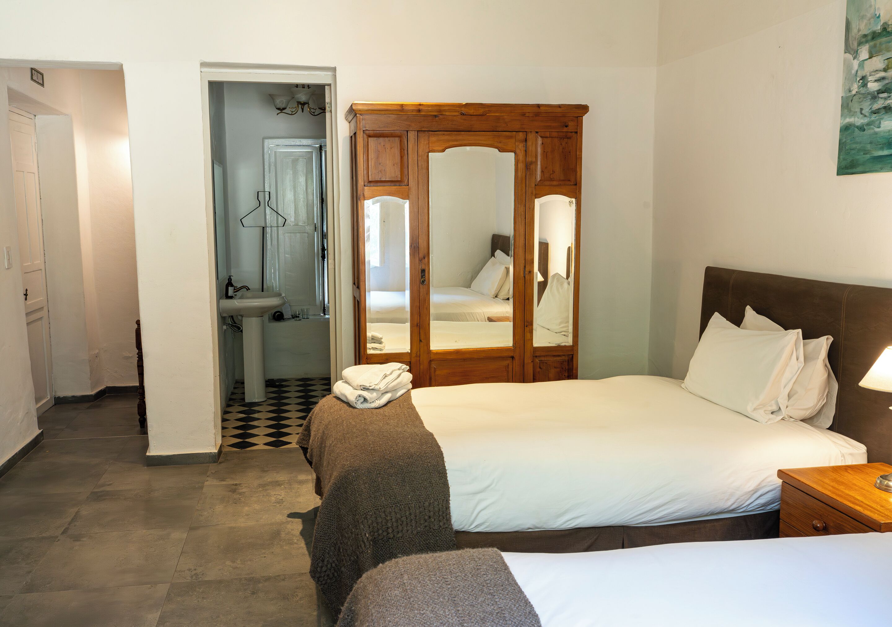 Quarto com cama, guarda-roupa de madeira, espelho e banheiro com pia e vaso sanitário.