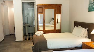 Quarto com cama, guarda-roupa de madeira, espelho e banheiro com pia e vaso sanitário.