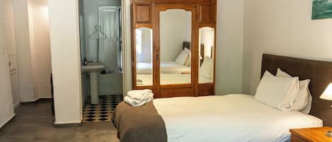 A bedroom with a bed, a wooden wardrobe, a mirror, and a bathroom with a sink and toilet.