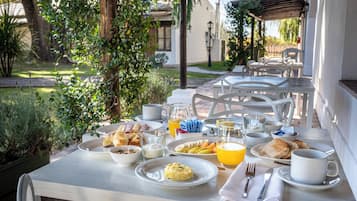 A breakfast table set outdoors with plates of food, a glass of orange juice, and a cup.