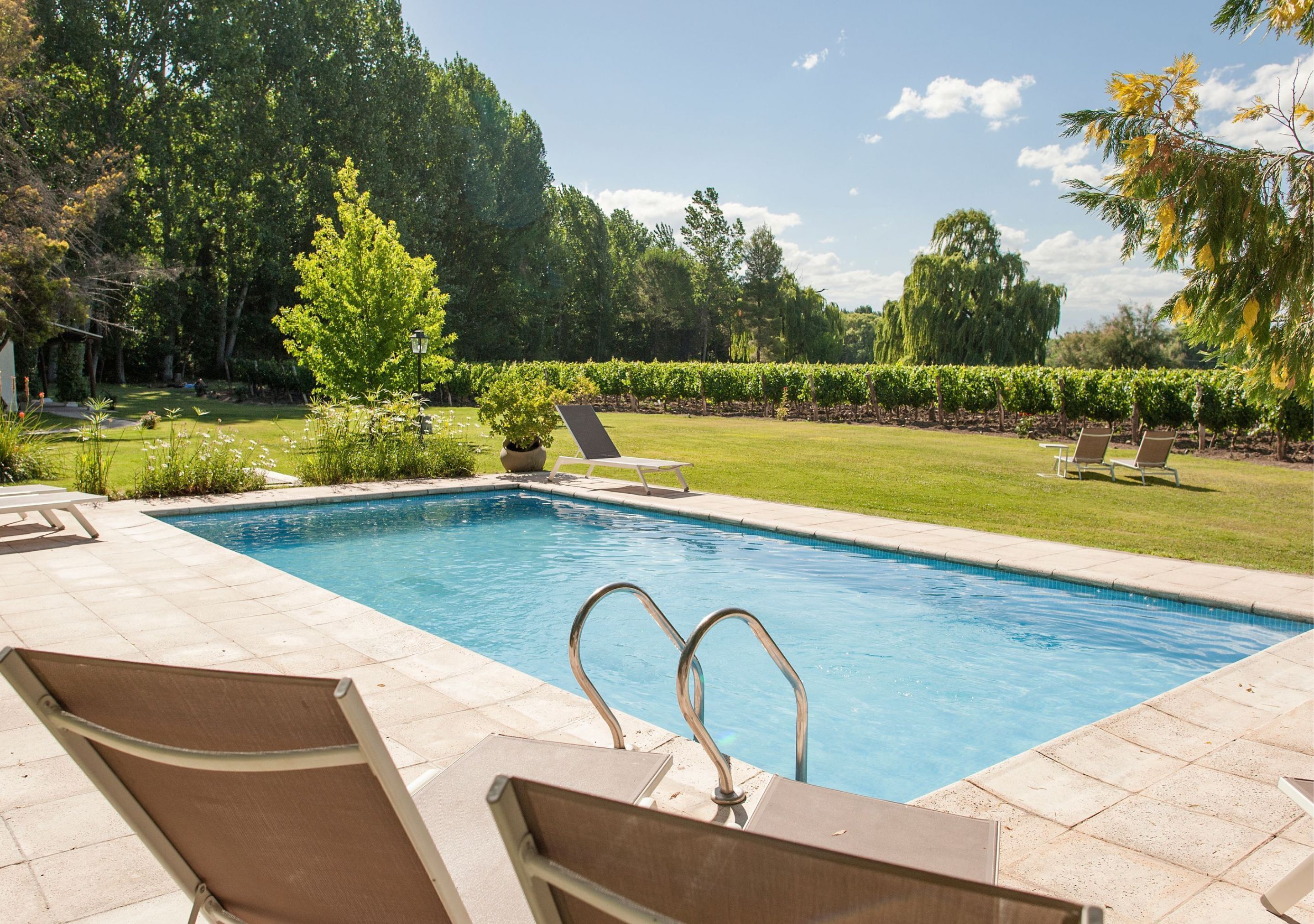 Una piscina con sillones de descanso y un césped bien cuidado.