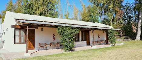 A single-story building with a flat roof, a covered porch with chairs, and a small tree in front.