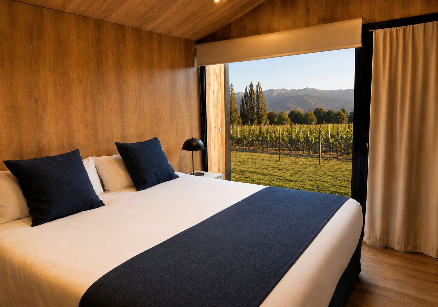 A bedroom with a large bed, two pillows, a bedside lamp, and a view of a vineyard through a window.