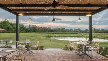 An outdoor patio with tables and chairs, a ceiling fan, and a view of a pond and trees.