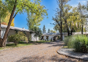A gravel driveway leading to a building with a covered patio area, surrounded by trees and greenery.