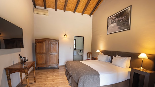 A bedroom with a wooden floor, a bed with pillows, a nightstand with a lamp, a wooden wardrobe, and a framed picture on the wall. - Postales Finca & Bodega by DOT Boutique (Tunuyan)