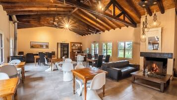 Un salón amplio con chimenea, vigas de madera en el techo y un comedor con sillas blancas y una mesa de madera.