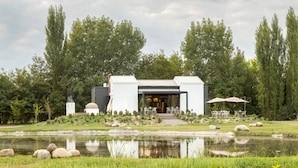 A modern building with a glass facade, surrounded by a pond and greenery. - Postales Finca & Bodega by DOT Boutique (Tunuyan)