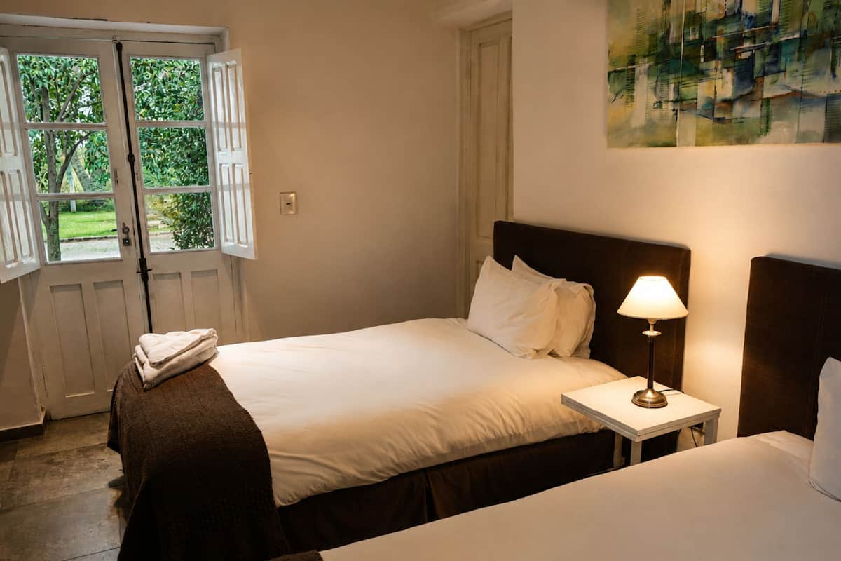 Ein Schlafzimmer mit Bett, Nachttisch mit Lampe, Fenster mit Rollläden und einem Bild an der Wand.