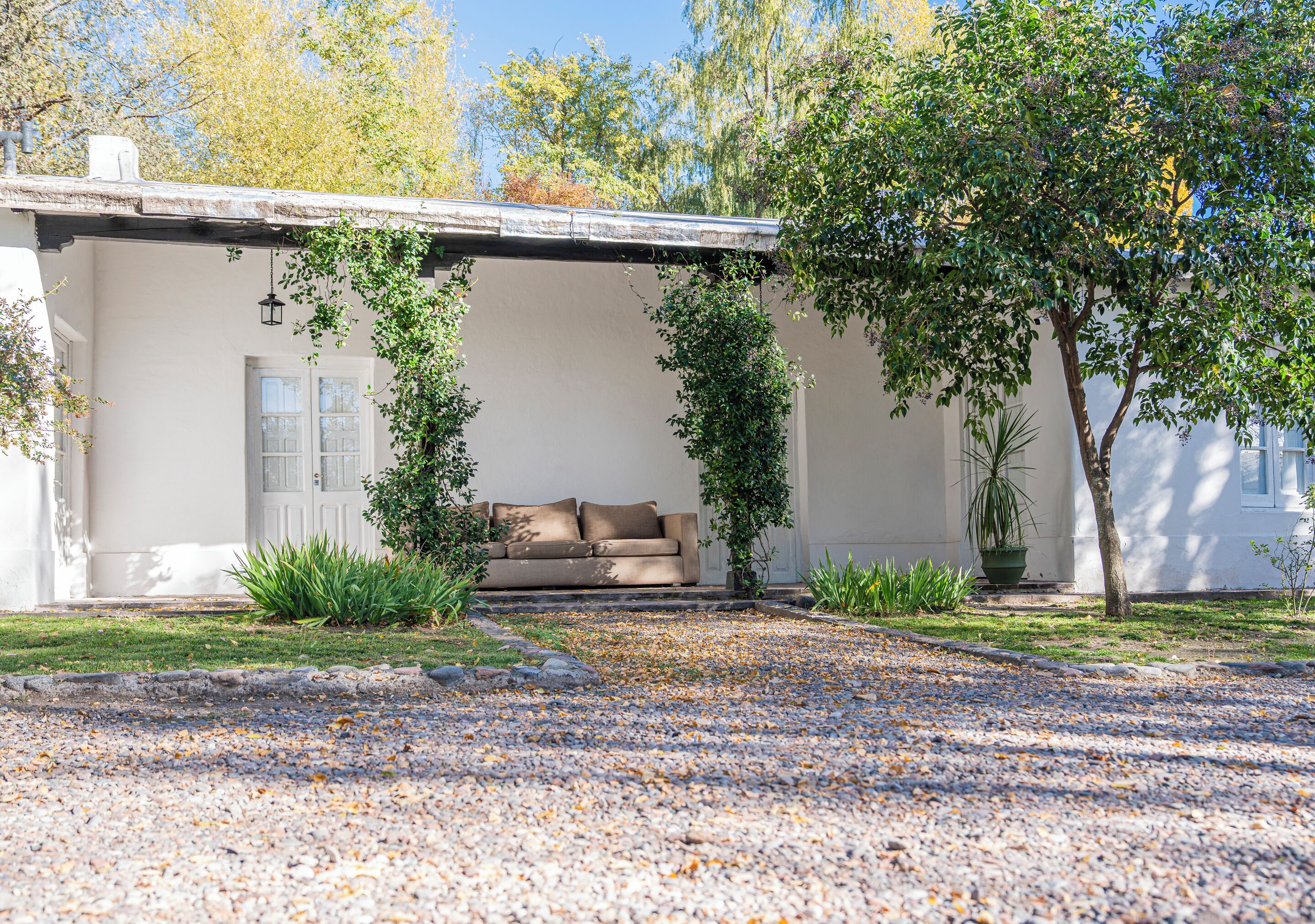 A covered outdoor seating area with a sofa, a door, and potted plants.