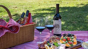 A picnic setup with a basket, wine bottle, glasses, and a pizza on a checkered tablecloth.