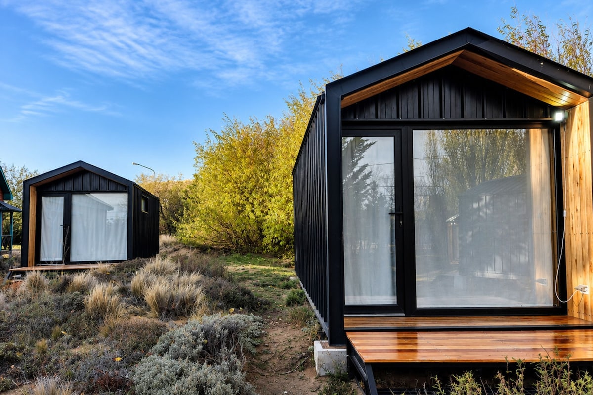 Two modern cabins with large windows, wooden decks, and a natural landscape.