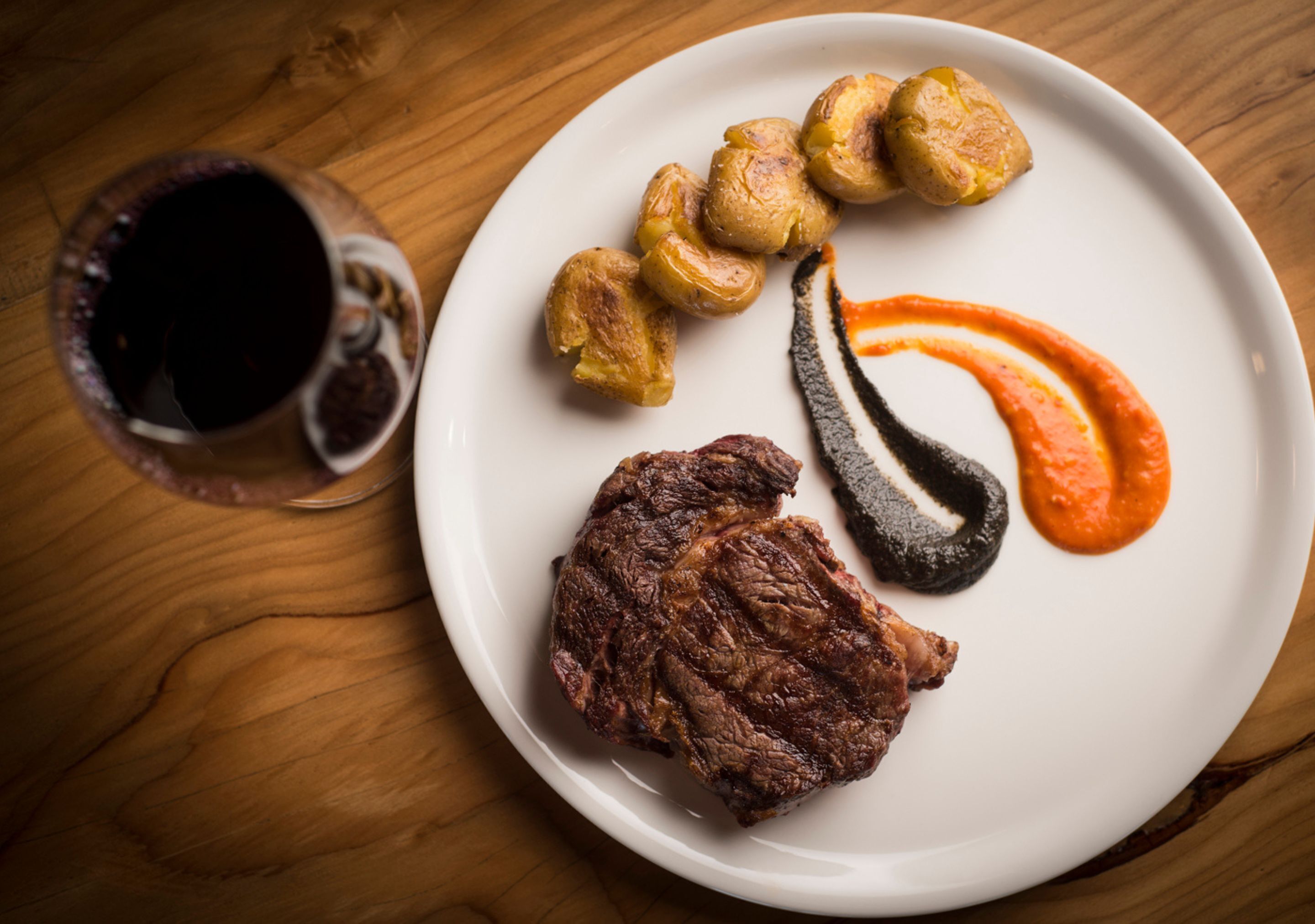 Une assiette contenant un steak, des pommes de terre rôties et différentes sauces, le tout posé sur une table en bois.