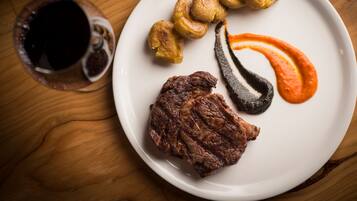 Une assiette contenant un steak, des pommes de terre rôties et différentes sauces, le tout posé sur une table en bois.