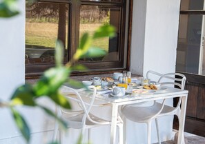A breakfast table set with plates, cups, and a glass of orange juice, positioned near a window with a view of a grassy area. - Postales Finca & Bodega by DOT Boutique (Tunuyan)