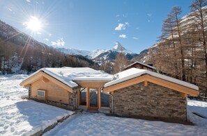 A wooden cabin with a stone extension, surrounded by snow-covered landscape and mountains.