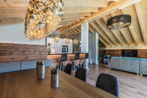 A modern kitchen with wooden beams, a dining area with a wooden table and chairs, and a living area with a sofa and TV.