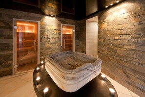 A stone bathtub in a spa area with two glass doors and a stone wall backdrop. - Hotel Hemizeus & Iremia Spa (Zermatt)