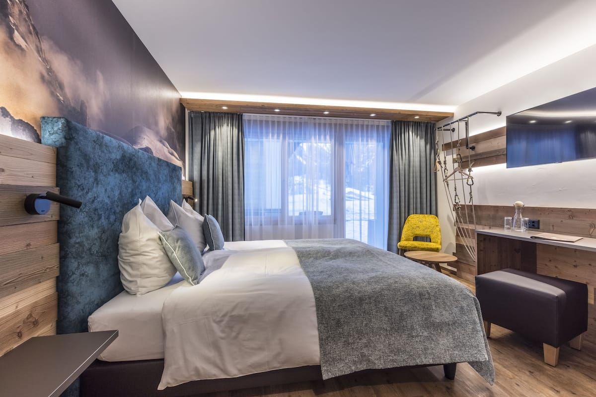 Ett modernt hotellrum med en stor säng, ett skrivbord, en stol och en tv som är monterad på väggen.