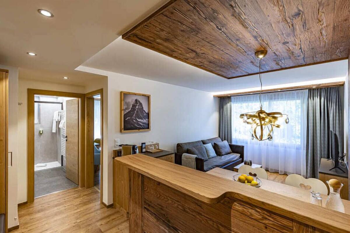 Ett modernt vardagsrum med ett träpanelat tak, en soffa, ett matbord och ett stort fönster med gardiner.