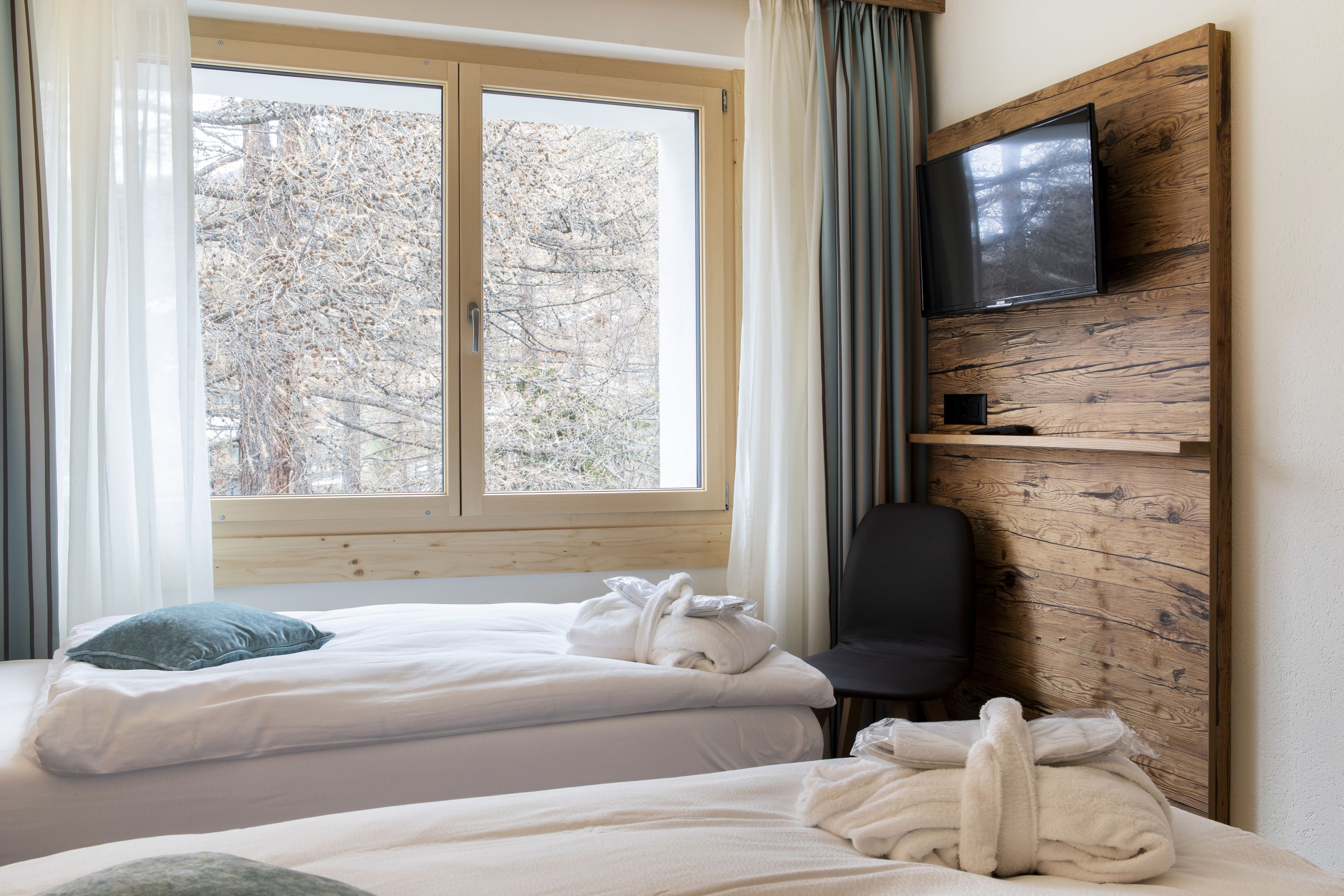 Habitació d'hotel amb dos llits, un televisor fixat a una paret de fusta i una finestra que donar a arbres.