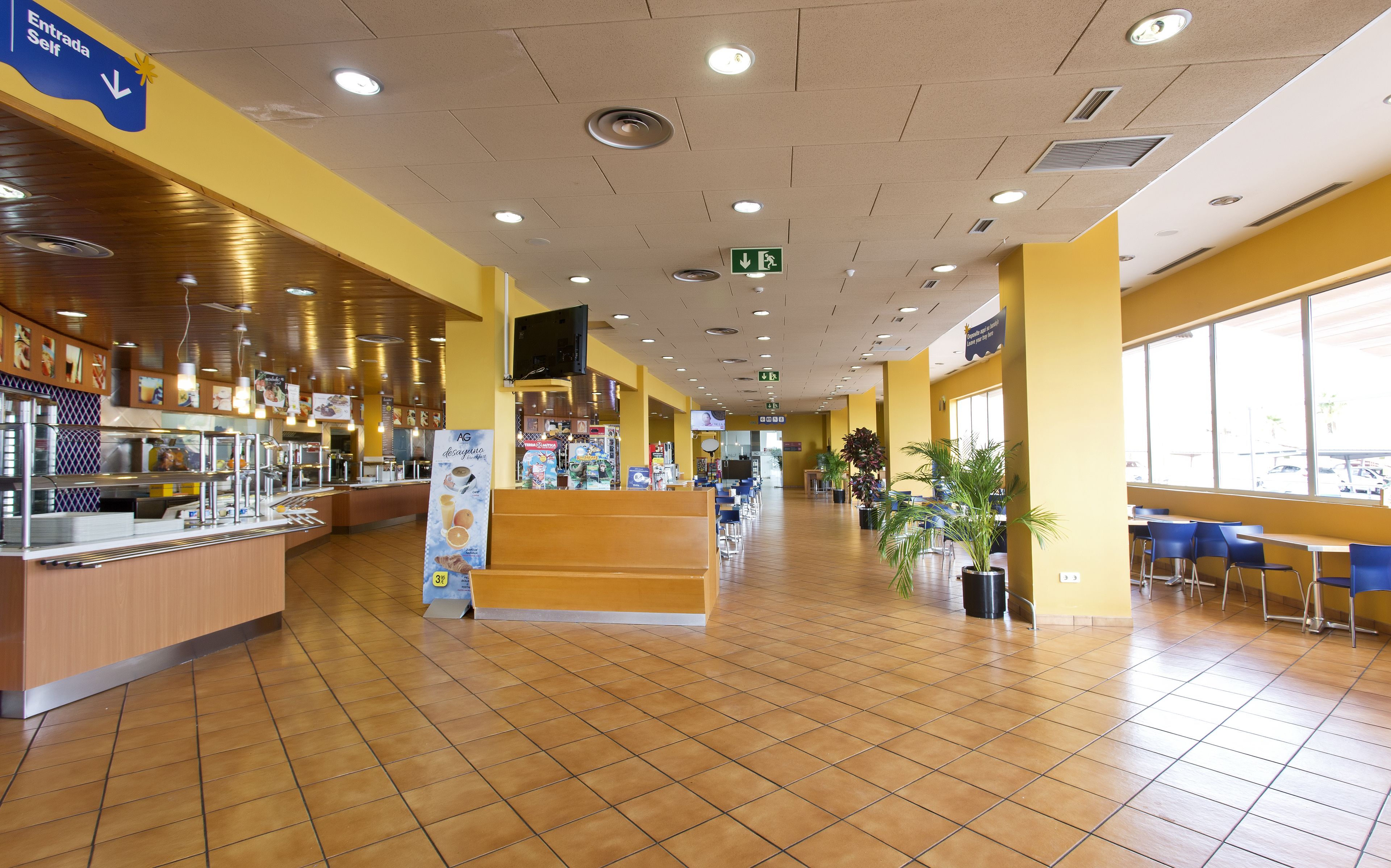 Una amplia cafetería con una barra larga, zona de estar y ventanas grandes.