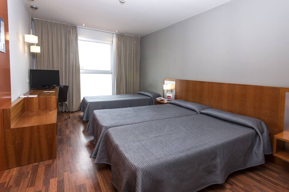 A hotel room with two beds, a desk with a computer, a TV, and a window with curtains.