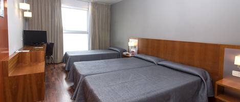 Ein Hotelzimmer mit zwei Betten, einem Schreibtisch mit Computer, einem Fernseher und einem Fenster mit Vorhängen.