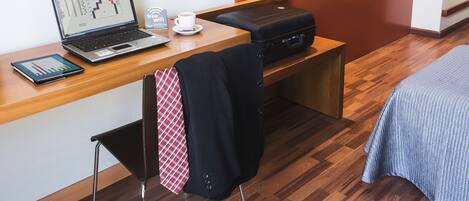 Habitación de hotel con un escritorio de madera, una computadora portátil, un teléfono inteligente, una maleta y una cama con una manta azul.