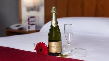Een fles Jaume Serra cava wijn, een glas en een rode bloem op een bed met witte lakens.
