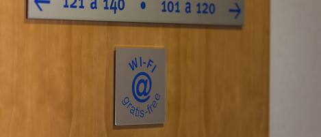 Un letrero con indicaciones hacia las habitaciones 121-140 y 101-120, y un símbolo de Wi-Fi que indica acceso gratuito a internet.