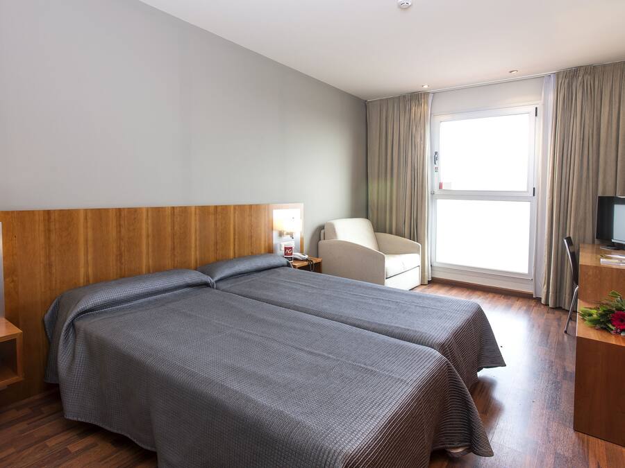 A hotel room with two beds, a desk with a computer, a chair, a TV, and a window with curtains.