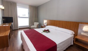 A hotel room with a large bed, a desk, a chair, a TV, and a window with curtains. - Hotel AG Express Elche (Elche)