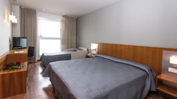 A hotel room with two beds, a desk with a computer, a TV, and a window with curtains.