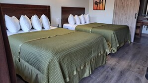A hotel room with two beds, each with white pillows and green bedspreads. There is a painting of palm trees on the wall, and a sliding door to the right. - Dunes Motel (Bend)