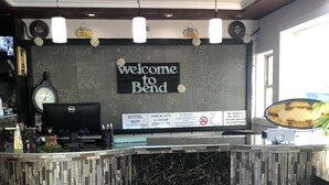 A reception desk with a 'Welcome to Bend' sign, a clock, and a Dell computer monitor. - Dunes Motel (Bend)